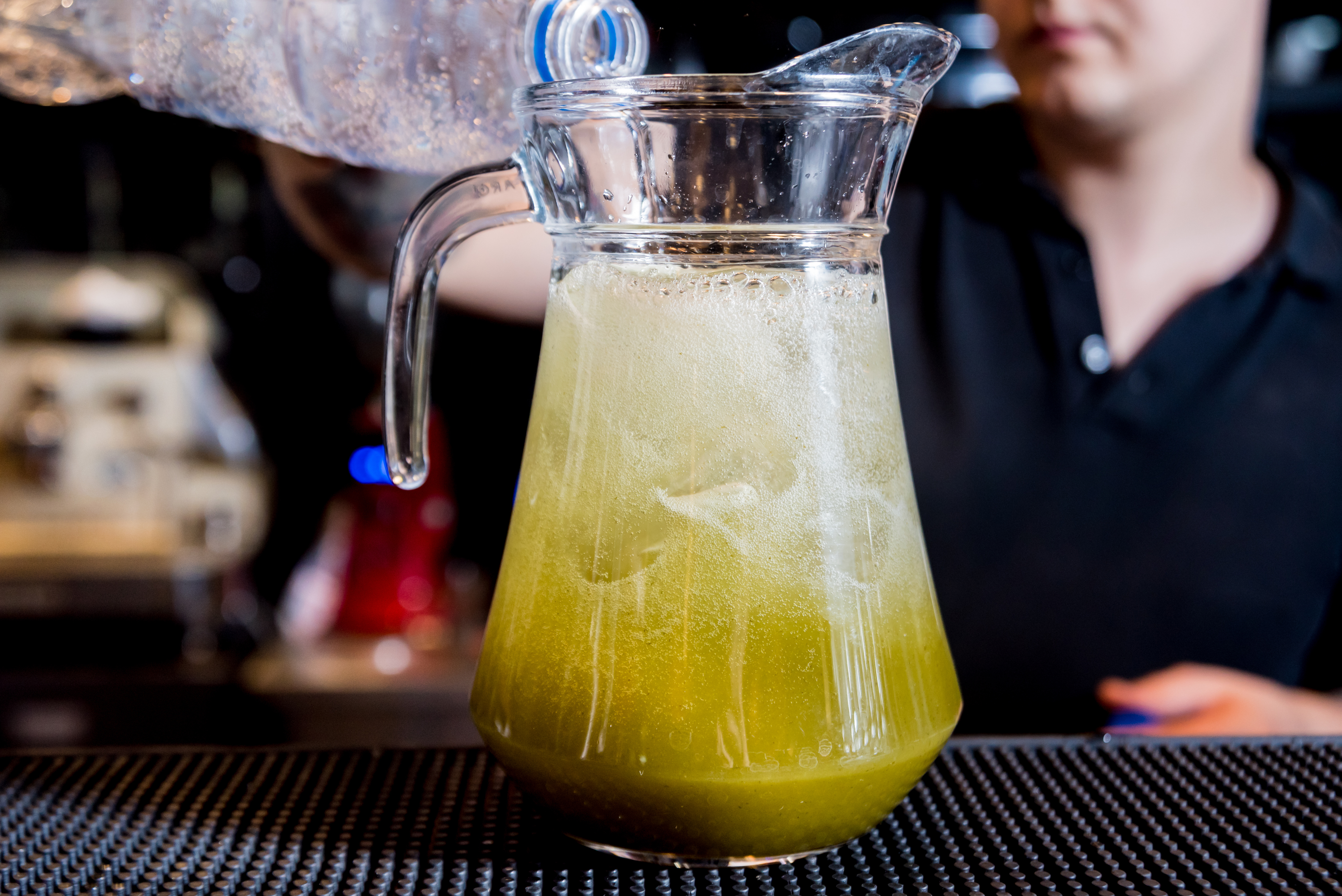 Bartender pouring a batched frozen cocktail from a pitcher behind the bar