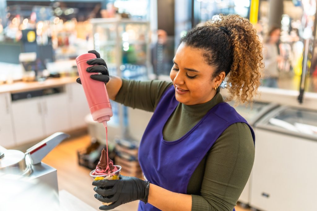 A food service worker preparing a frozen dessert behind a counter