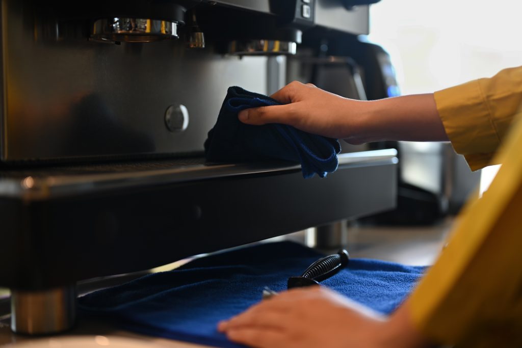 A barista cleaning a commercial beverage machine at a cafe counter