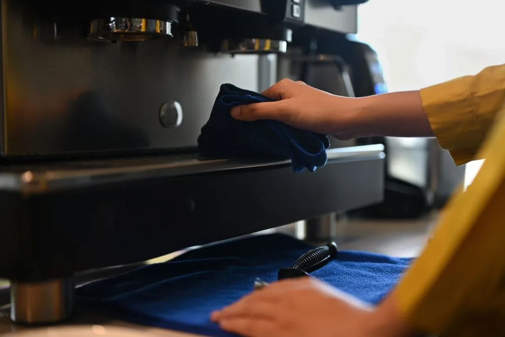 A barista cleaning a commercial beverage machine at a cafe counter