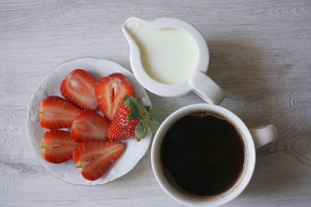 Overhead view of fresh strawberries, cream, and a cup of coffee.