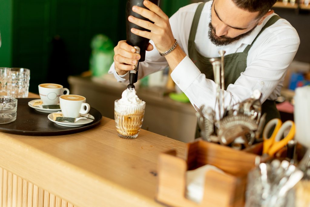 Barista garnishing a seasonal holiday drink with whipped cream.