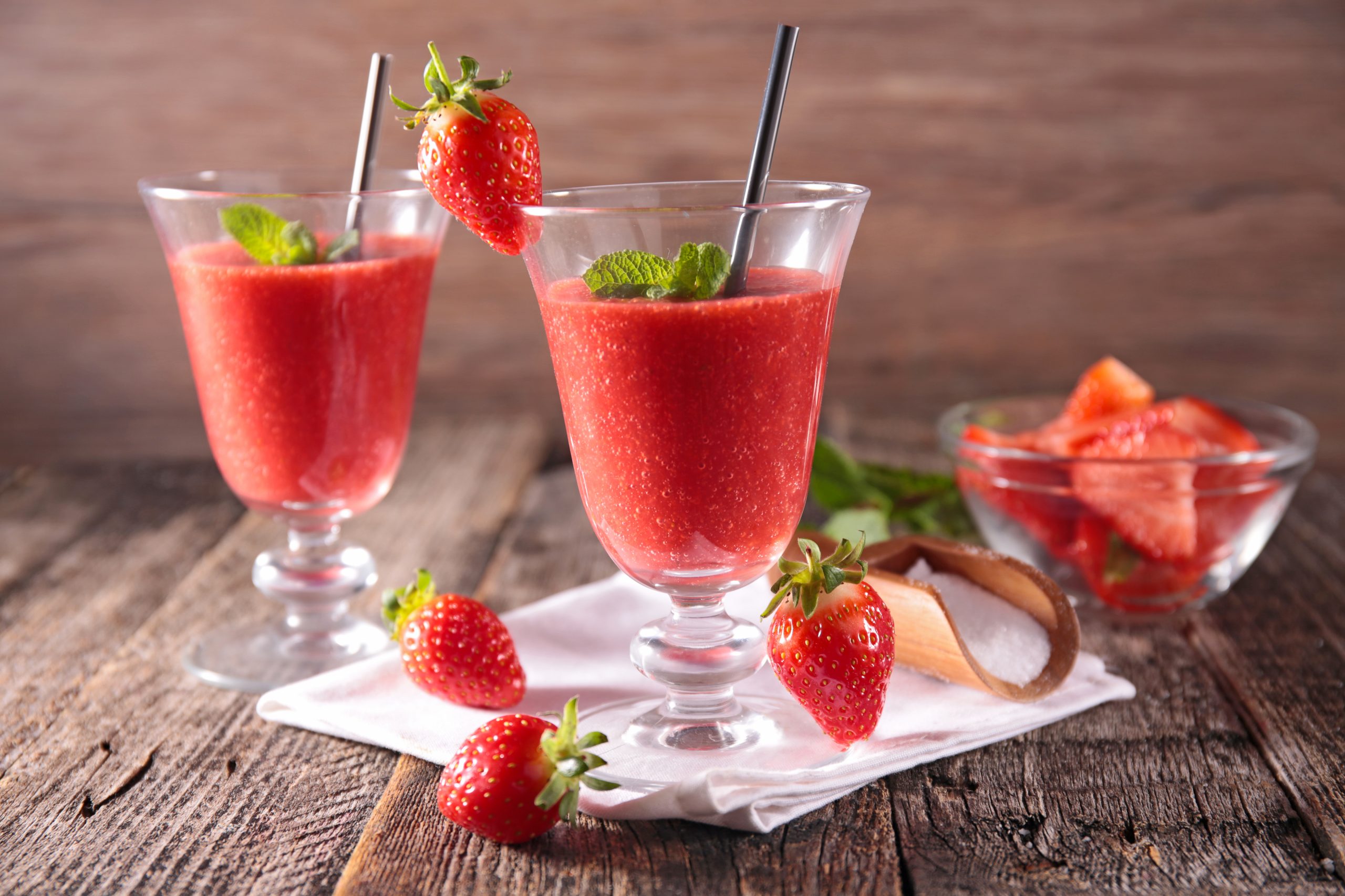 Strawberry smoothie, strawberry frappe, and frozen strawberry cocktail lined up on a counter with fresh strawberries