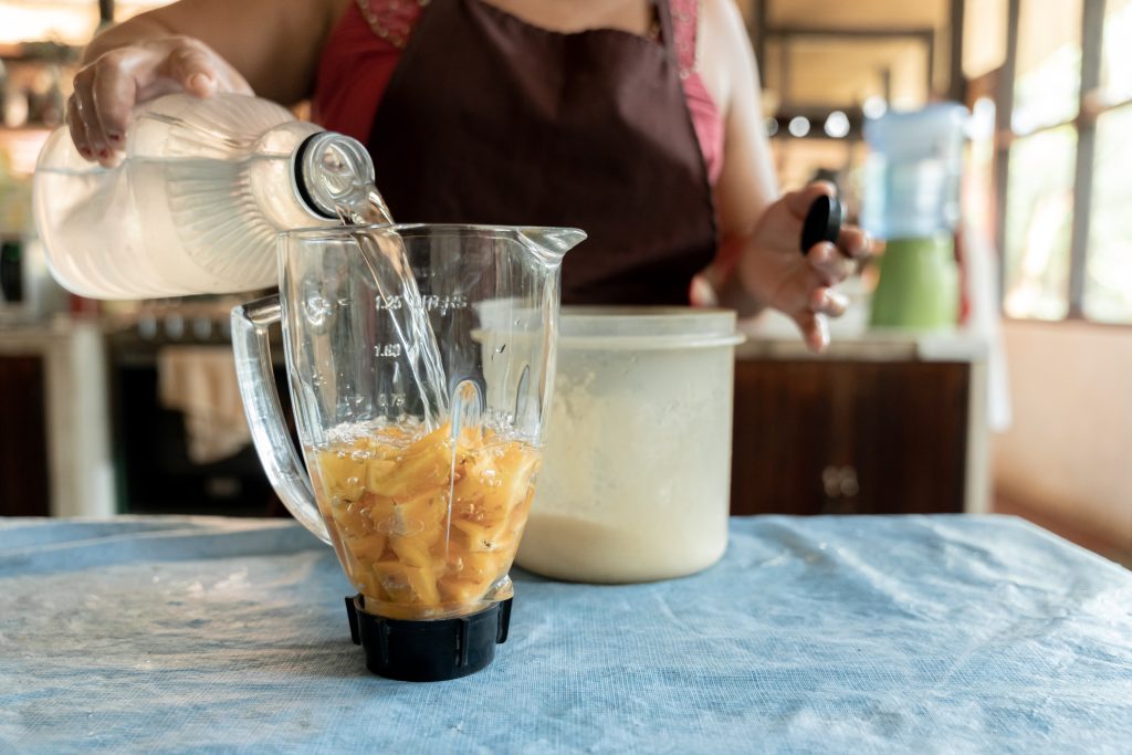 Barista pouring strawberry concentrate into a blender pitcher filled with ice